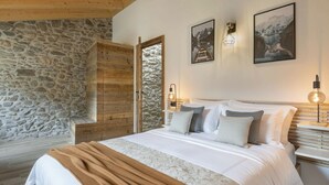 Ein Schlafzimmer mit Steinswand, Holzboden, einem Bett mit weißer Bettwäsche, zwei Wandleuchten und zwei gerahmten Bildern.
