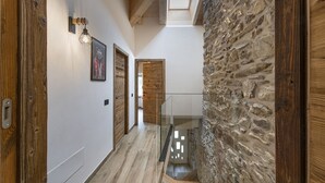 Ein Flur mit Holzdielen, einer Steinwand und einem Glasgeländer, das zu einer Treppe führt.