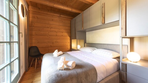 A bedroom with a wooden ceiling, a bed with white bedding, a chair, and bedside lamps.