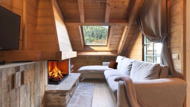 Une chambre confortable située dans les combles, avec une cheminée en pierre, un canapé et un téléviseur fixé au mur.