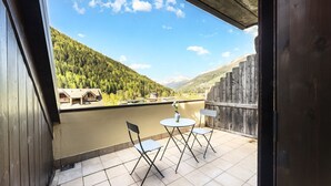 Un balcon avec vue sur une rivière, une terrasse en bois et une chaîne de montagnes en arrière-plan.