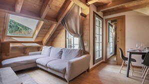 Une pièce chaleureuse avec un plafond en bois, un canapé gris, une table à manger avec des chaises et de grandes fenêtres avec des rideaux.