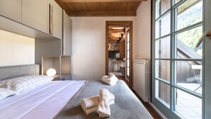 Une chambre avec une grande fenêtre, un lit avec des oreillers, une table de chevet et une vue sur une cuisine et un balcon.