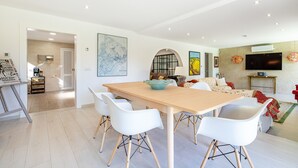 Un salon moderne avec un coin repas, comprenant une grande table en bois, des chaises blanches et un canapé.