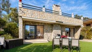 Une maison moderne avec des murs en pierre, un balcon et une terrasse aménagée avec du mobilier d’extérieur.