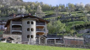 A stone building with multiple balconies, surrounded by lush greenery and other buildings in a hilly area. - Eden View - Two Bedroom Apartment, Sleeps 6 (Monno)