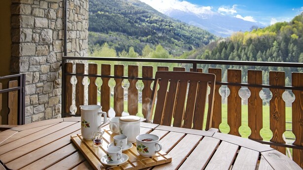 A wooden table with a tray of tea set on a balcony with a stone wall and a view of a forested mountain range. - Eden View - Two Bedroom Apartment, Sleeps 6 (Monno)