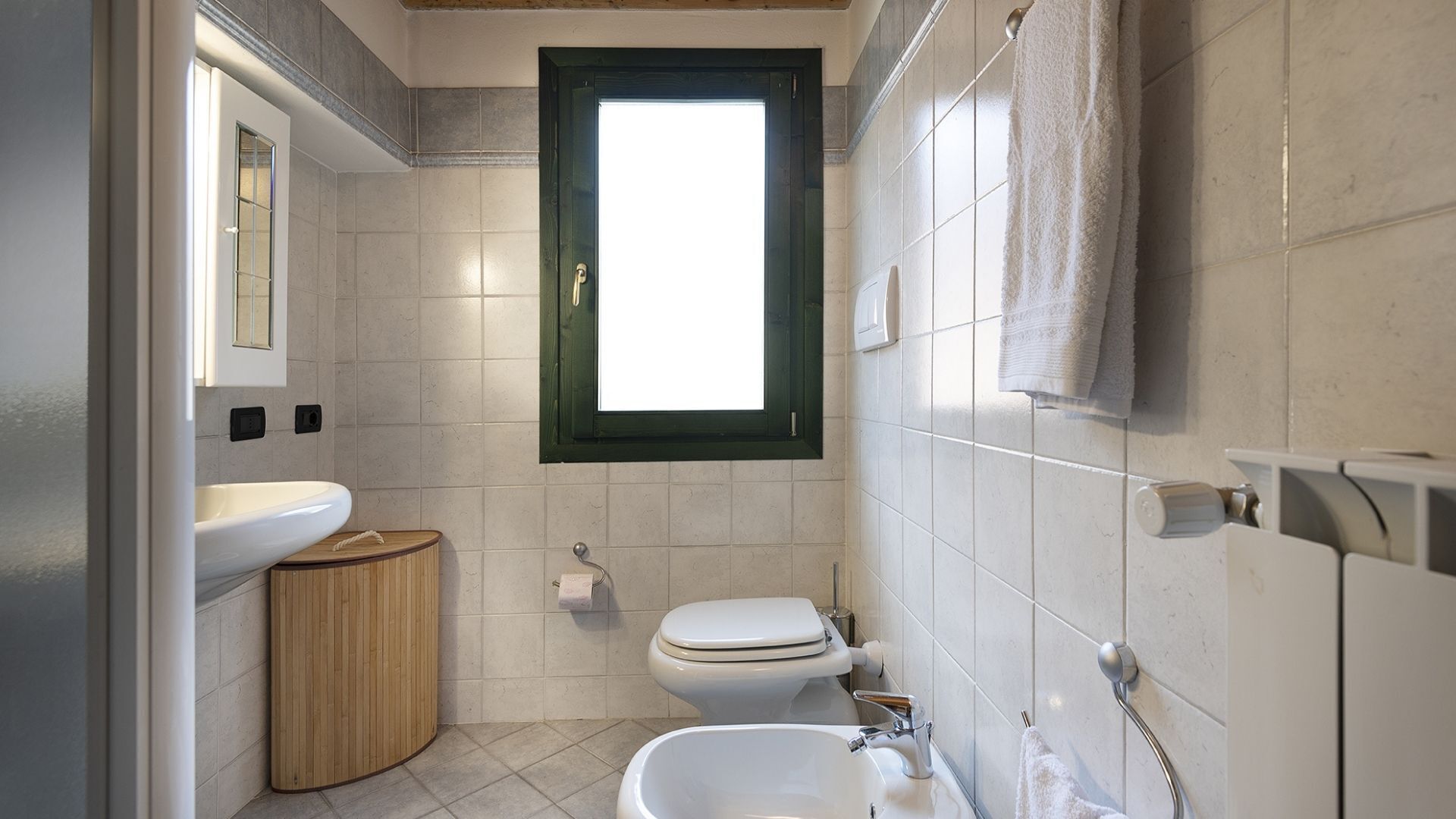 A bathroom with a toilet, bidet, sink, and a window.