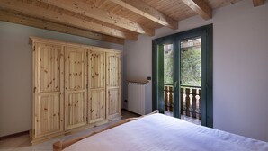 A bedroom with a wooden wardrobe, a bed, and a balcony with a green door. - Eden View - Two Bedroom Apartment, Sleeps 6 (Monno)