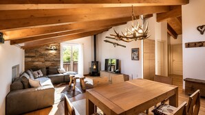 Un salon chaleureux avec un mur en pierre, des poutres apparentes en bois au plafond, une cheminée, une table à manger et un canapé.