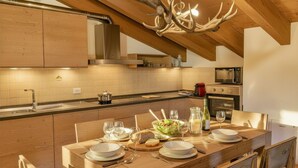 Une cuisine moderne avec des meubles en bois, un îlot central aménagé en coin repas, des appareils en acier inoxydable et un lustre original en forme de bois de cerf.