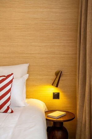 Quarto de hotel com cama, luminária de cabeceira, mesa de apoio e cortina.