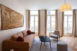 Uma sala de estar com sofá, poltrona, mesa de centro e um quadro na parede.