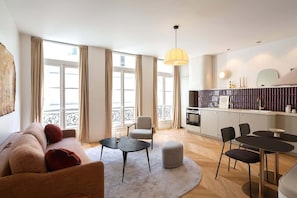 Uma sala de estar moderna com sofá, duas poltronas, uma mesa redonda e um espaço de cozinha com mesa e cadeiras.