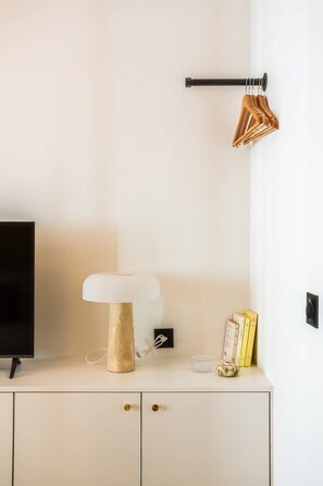 Quarto moderno com armário branco, TV de tela plana, luminária e porta-roupas fixado na parede.