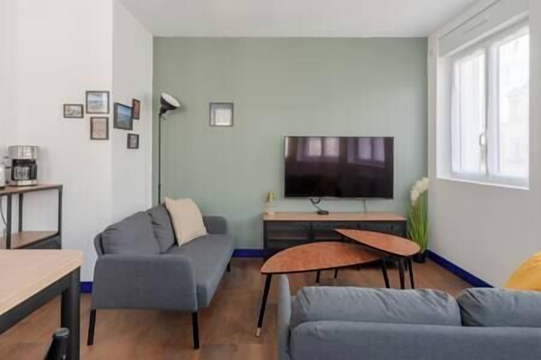 A modern living room with a grey sofa, a coffee table, and a flat-screen TV mounted on the wall.