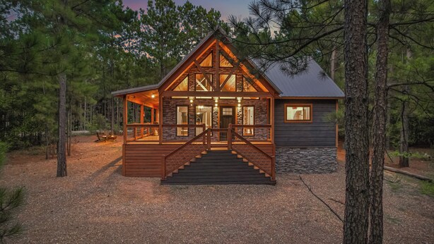 A cabin with a stone foundation, wooden exterior, and a staircase leading to the entrance. - Romantic Cabin Swings | Private Sauna & Hot Tub! (Broken Bow)