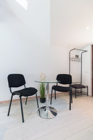 Simple seating area with a round table and two chairs, complemented by a potted plant and a sleek metal rack.
