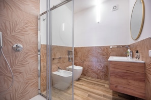 Un bagno con box doccia in vetro, un bidet, un water, un lavabo con specchio e pavimento in legno.