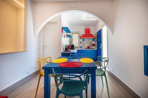 Una cucina moderna con isola centrale, zona pranzo con sottopiatti colorati e vista sulla sala da pranzo adiacente.