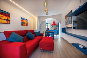 A modern living room with a red sofa, a dining area with a blue table, and a kitchen visible through an archway.
