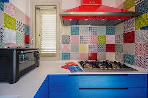 A kitchen with a microwave, gas stove, and a variety of colorful tiles on the backsplash.