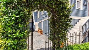 A gated entrance with a metal gate, a gravel path, and a staircase leading to a building with blue siding and white trim. - Bamboo & Clover - Historic Galveston Cottage (Galveston)