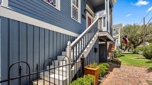 A two-story house with a blue exterior, a brick pathway, and a small garden area. - Bamboo & Clover - Historic Galveston Cottage (Galveston)