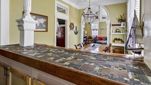 A spacious kitchen with a large island, a chandelier, and a view of the living area. - Bamboo & Clover - Historic Galveston Cottage (Galveston)