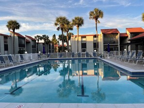 Ein Pool mit Liegestühlen und Palmen, umgeben von Gebäuden mit roten Dächern.