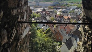 A view through a stone archway of a town with traditional buildings, a large industrial area, and a river in the distance. - Hermannstein Castle - Knights' Hall (Wetzlar)