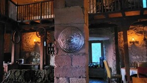 A rustic interior with stone walls, a wooden ceiling, and a stone fireplace. There is a balcony with a railing and a large clock on the wall. - Hermannstein Castle - Knights' Hall (Wetzlar)