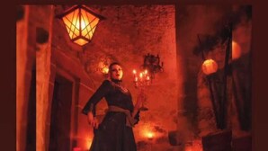 A person in a dark dress standing in a dimly lit room with a stone wall and a hanging lantern. - Hermannstein Castle - Knights' Hall (Wetzlar)