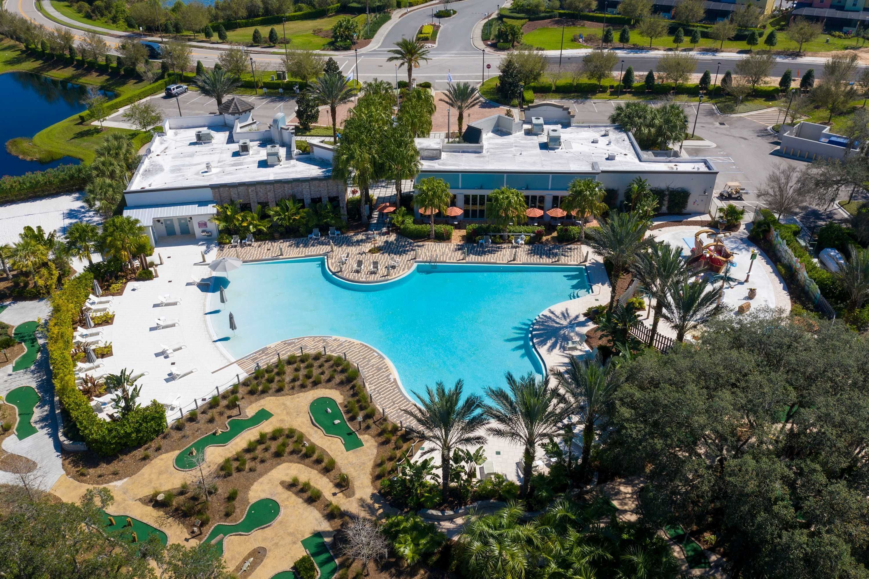 An aerial view of a resort with a large swimming pool, landscaped areas, and a parking lot.