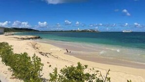 Ein Strand mit klarem türkisblauem Wasser, einem Sandufer und etwas Grün im Vordergrund.