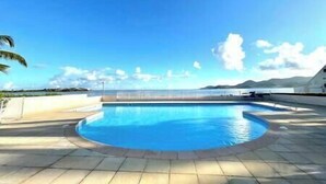 Ein Schwimmbecken mit geschwungener Kante, umgeben von einer gefliesten Terrasse, mit freiem Blick auf den Himmel und ferne Berge.
