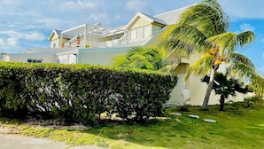 A two-story house with a white exterior, a covered patio, and a well-maintained lawn with palm trees. - Côté Mer - NBBC - 2 bedrooms beachfront (Marigot)