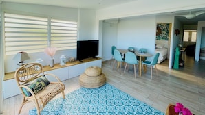 A modern living room with a TV, seating area, dining table, and a ceiling fan. - Côté Mer - NBBC - 2 bedrooms beachfront (Marigot)