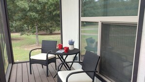 A covered outdoor seating area with wicker chairs and a table, overlooking a grassy yard. - 2-bedroom, pet friendly home with great amenities. It will be your happy place (Holly Lake Ranch)