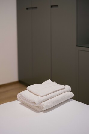 A stack of white towels on a white surface in a room with grey cabinets. - Casa Due Agosto Sleek and Central (Bologna)
