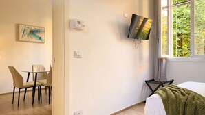 Hotelkamer met een bed, een aan de muur bevestigde televisie, een raam met uitzicht op bomen, een schilderij en een zithoek met een tafel en stoelen.