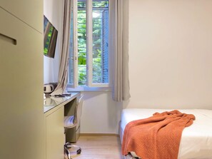 Une chambre à coucher avec un lit, un bureau avec un ordinateur, une chaise et une fenêtre avec des rideaux.