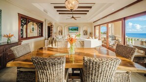 A spacious dining area with a large wooden table and wicker chairs, a ceiling fan, and a view of the ocean. - Panoramic Ocean-View, 4 BR, Luxe Penthouse Condo (Manuel Antonio)