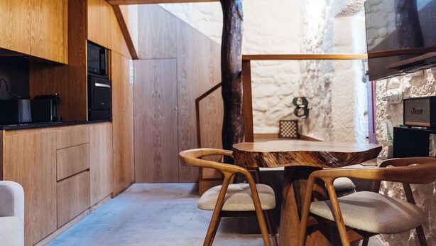 A compact kitchen with wooden cabinets, a dining table with chairs, and a stone wall.