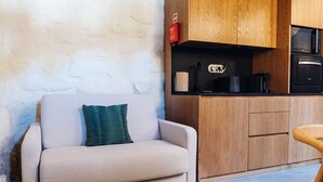 A compact living space with a sofa, a small kitchen area including a microwave and a coffee maker, and wooden cabinets.
