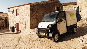 A compact delivery vehicle parked in front of a stone building with a tiled roof.