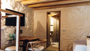A rustic room with a wooden dining table, chairs, a small shelf with items, and a door leading to a bathroom.