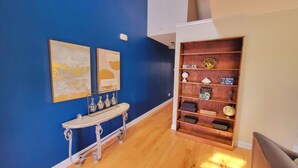 Un pasillo con pared azul, una consola blanca con jarrones y un estante de madera con diversos objetos.