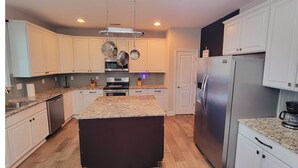 Cocina moderna con armarios blancos, encimeras de granito, electrodomésticos de acero inoxidable y una isla central.