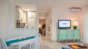 A dining area with a white table and chairs, a teal table runner, and a television on a teal cabinet. - Cozy Apartment by the Sea in Carboneras (Carboneras)